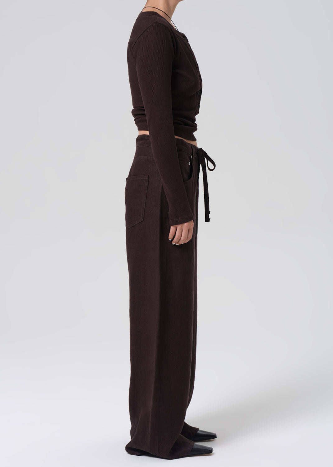 Person wearing a brown long-sleeve top and wide-leg pants on a grey background