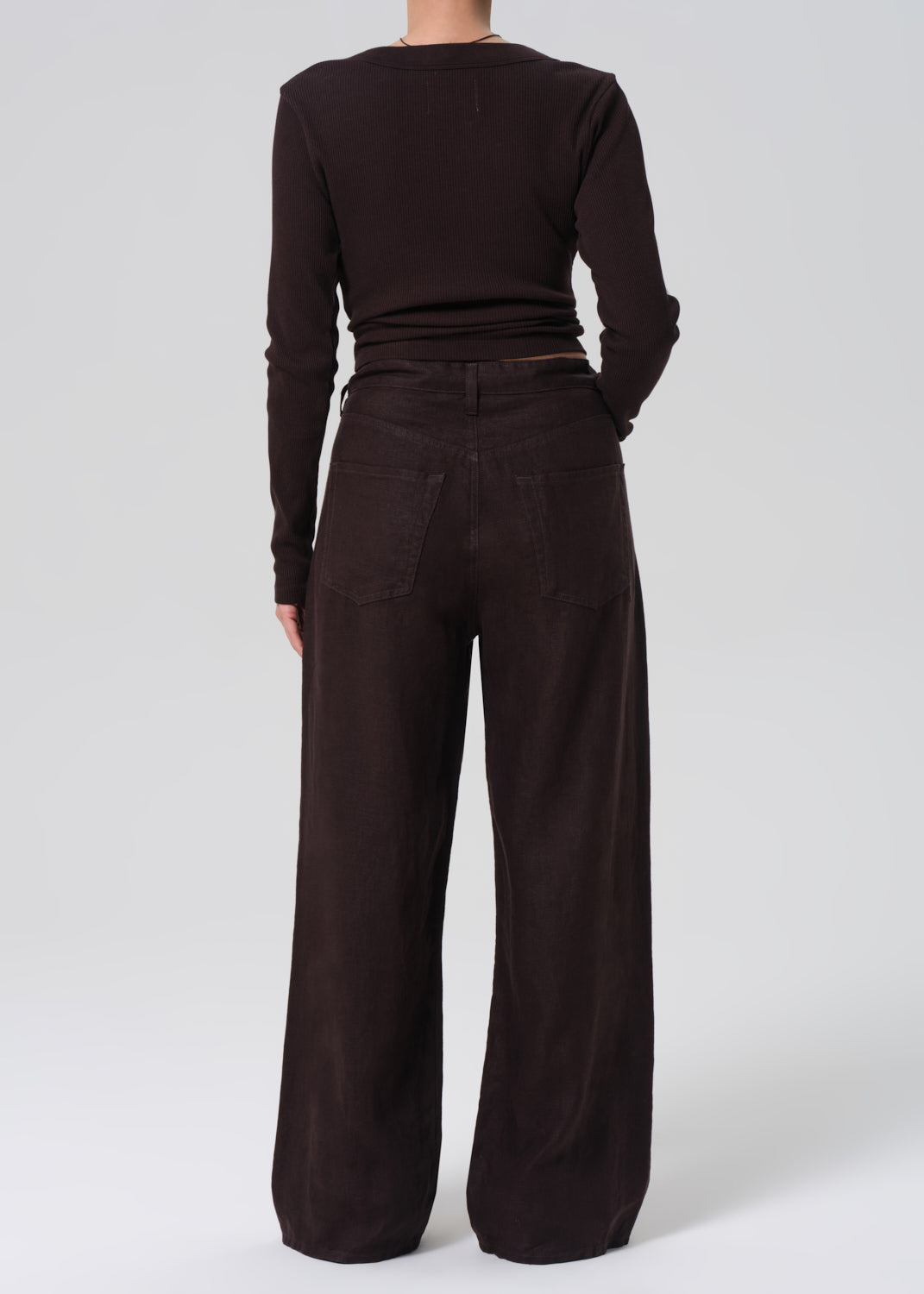 Person wearing a brown long-sleeve top and wide-leg pants on a grey background