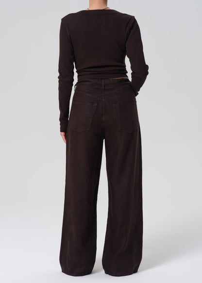 Person wearing a brown long-sleeve top and wide-leg pants on a grey background