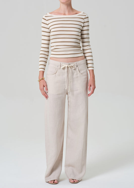 A model wearing a beige and brown horizontally striped long-sleeve crop top and light beige wide-leg linen pants with a drawstring waist, standing against a grey background.