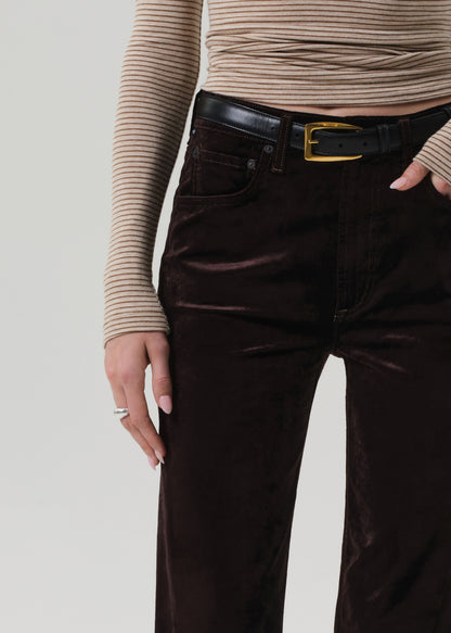 Person wearing a beige turtleneck and dark brown velvet pants on a grey background