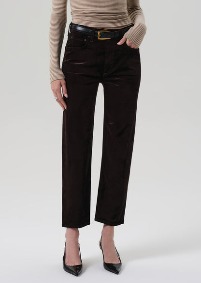 Person wearing a beige turtleneck and dark brown velvet pants on a grey background