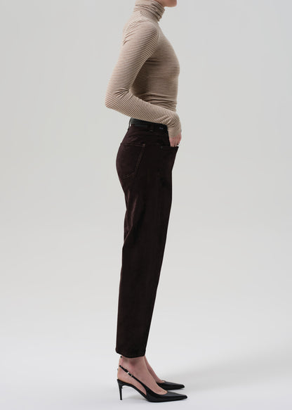 Person wearing a beige turtleneck and dark brown velvet pants on a grey background