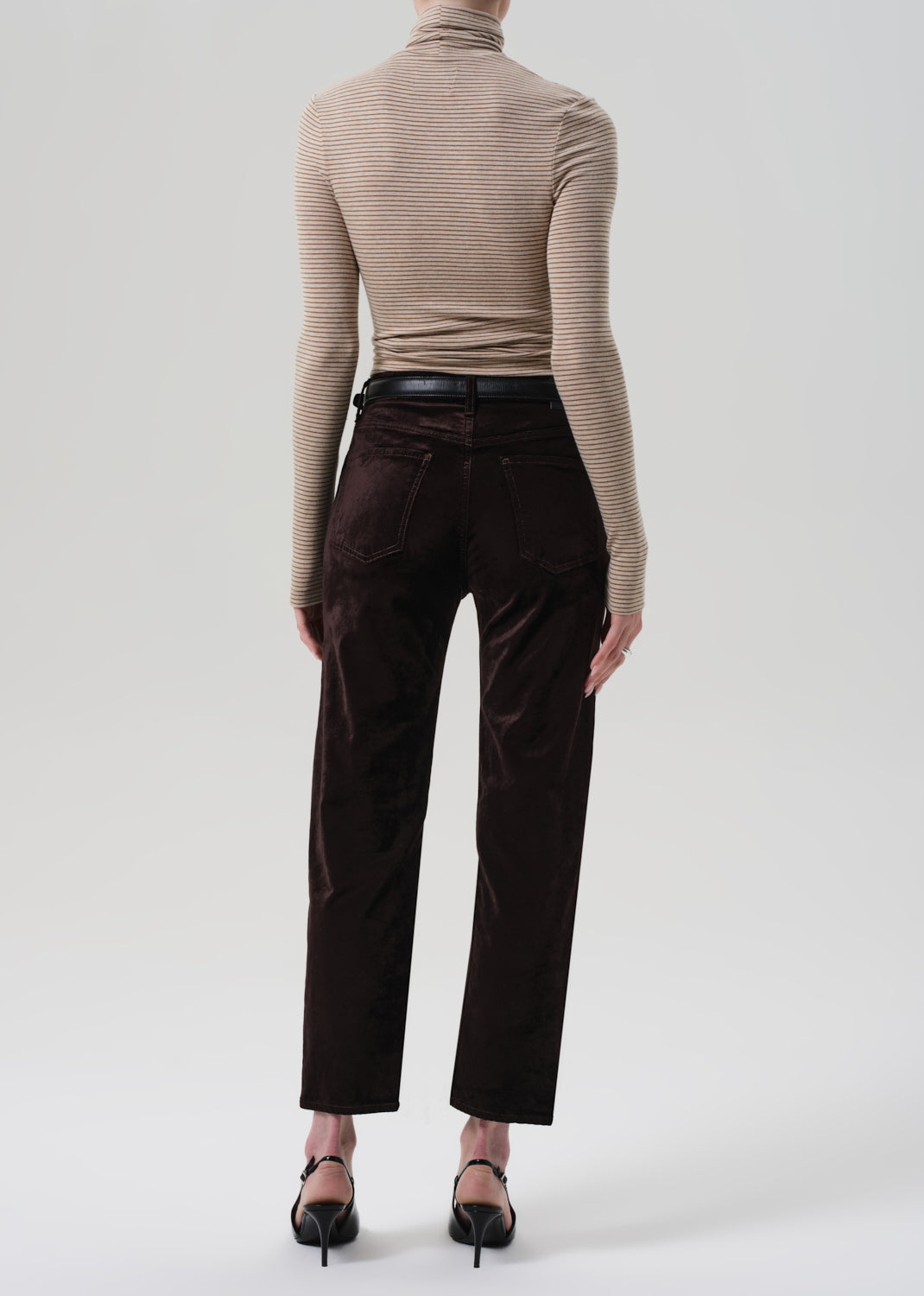 Person wearing a beige ribbed turtleneck and dark brown pants on a white background