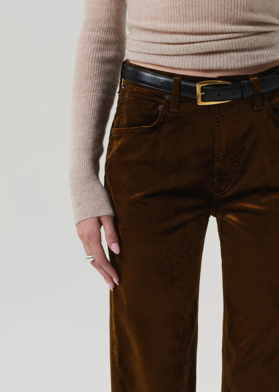 Person wearing a beige sweater and brown velvet pants on a grey background
