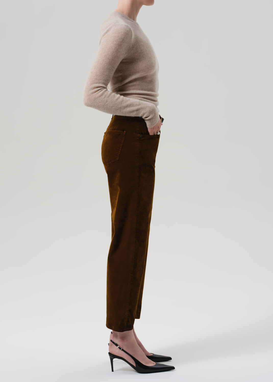 Person wearing a beige sweater and brown velvet pants on a grey background