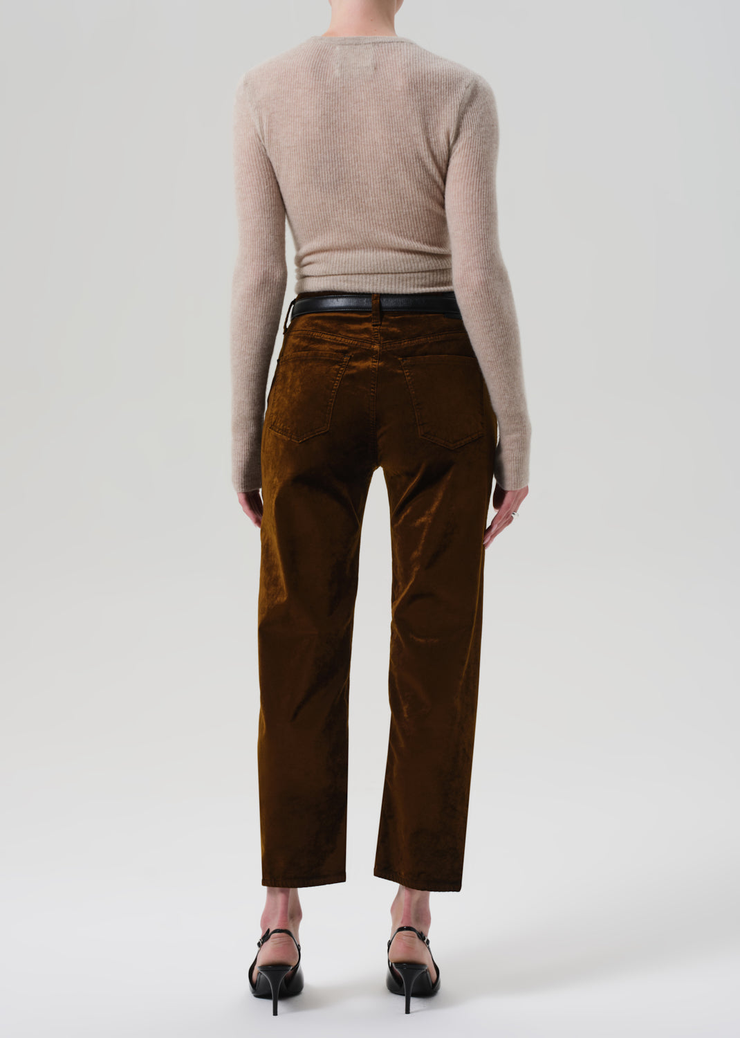 Person wearing a beige sweater and brown velvet pants on a grey background