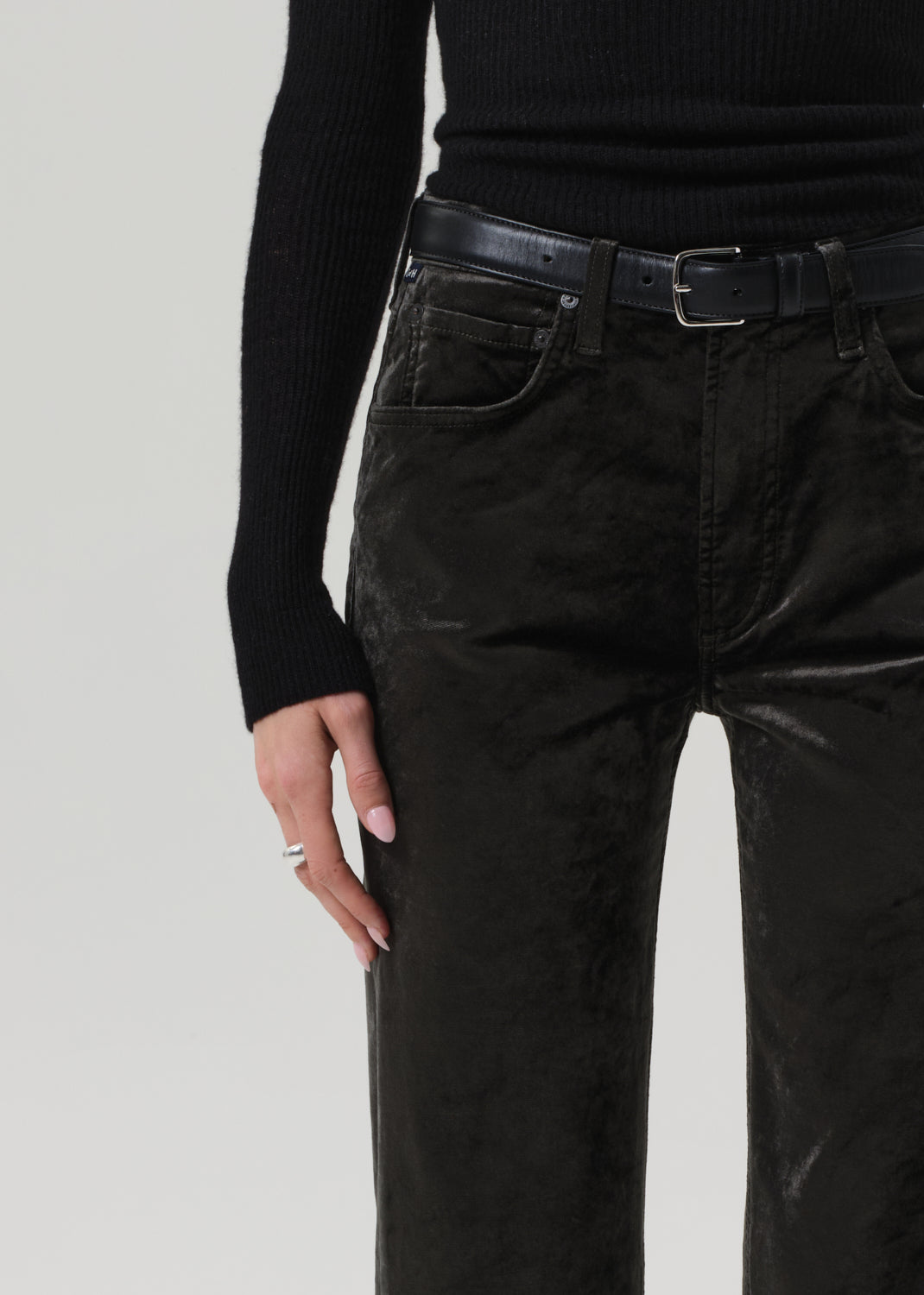 Person wearing a black turtleneck and green velvet pants on a grey background