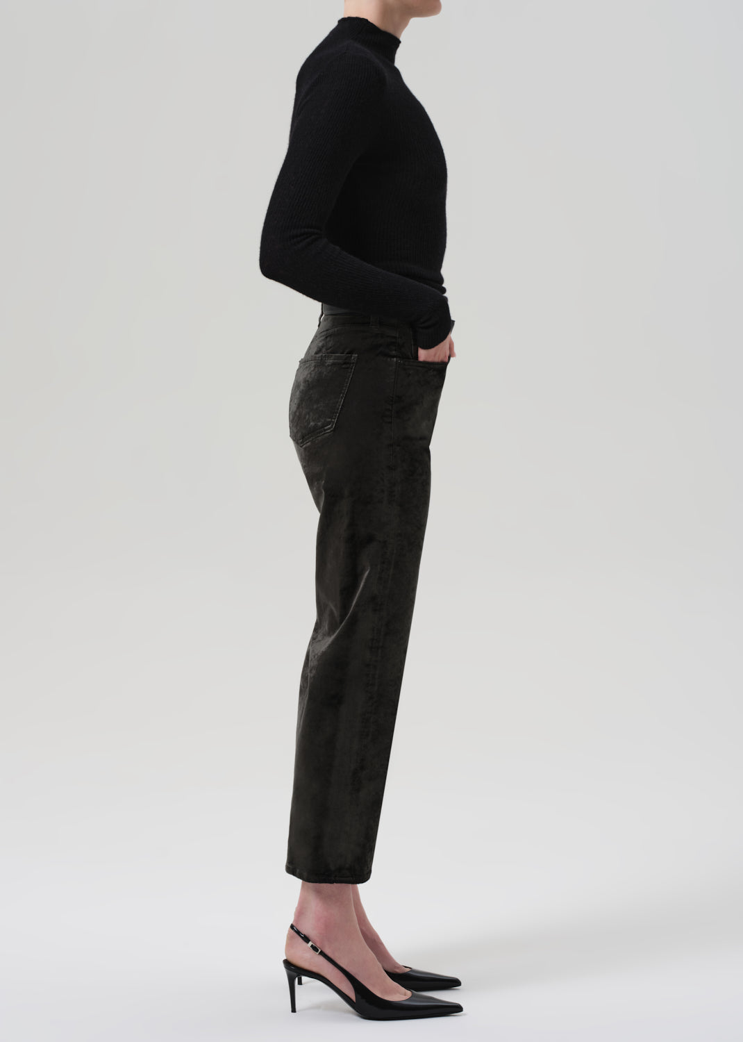 Person wearing a black turtleneck and green velvet pants on a grey background