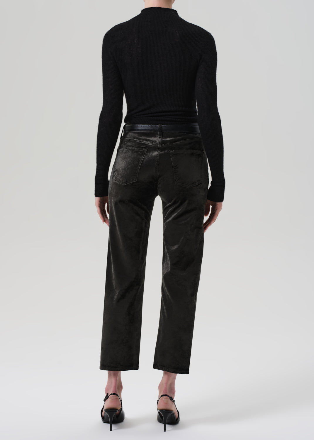 Person wearing a black turtleneck and green velvet pants on a grey background