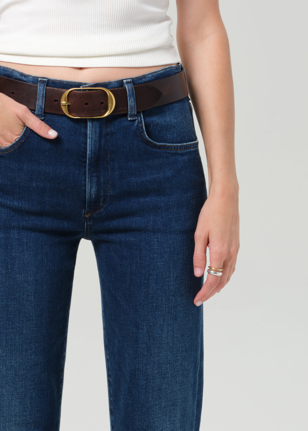 Person wearing blue jeans with a brown belt on a plain background