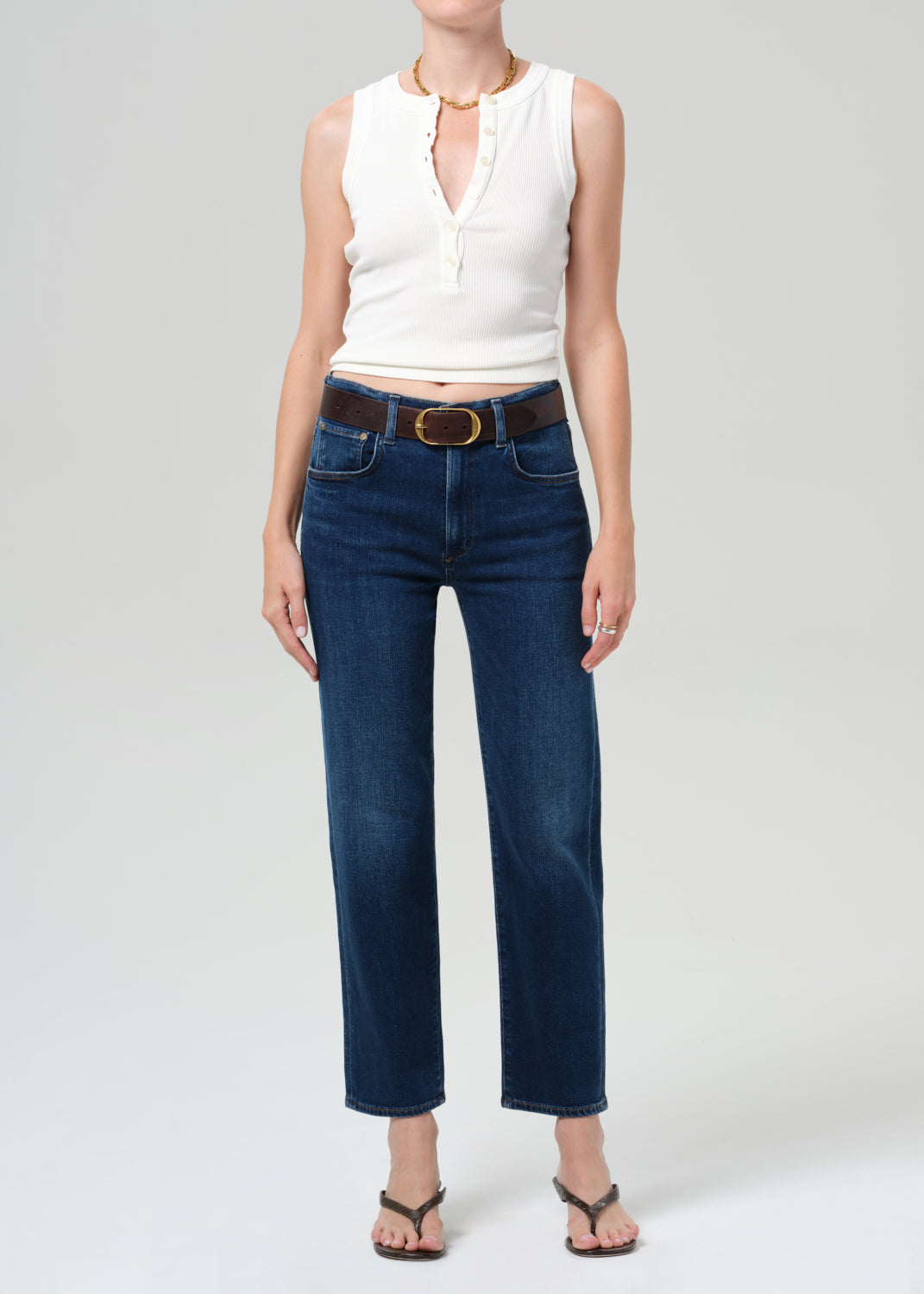 Person wearing a white sleeveless top and dark blue jeans on a light gray background