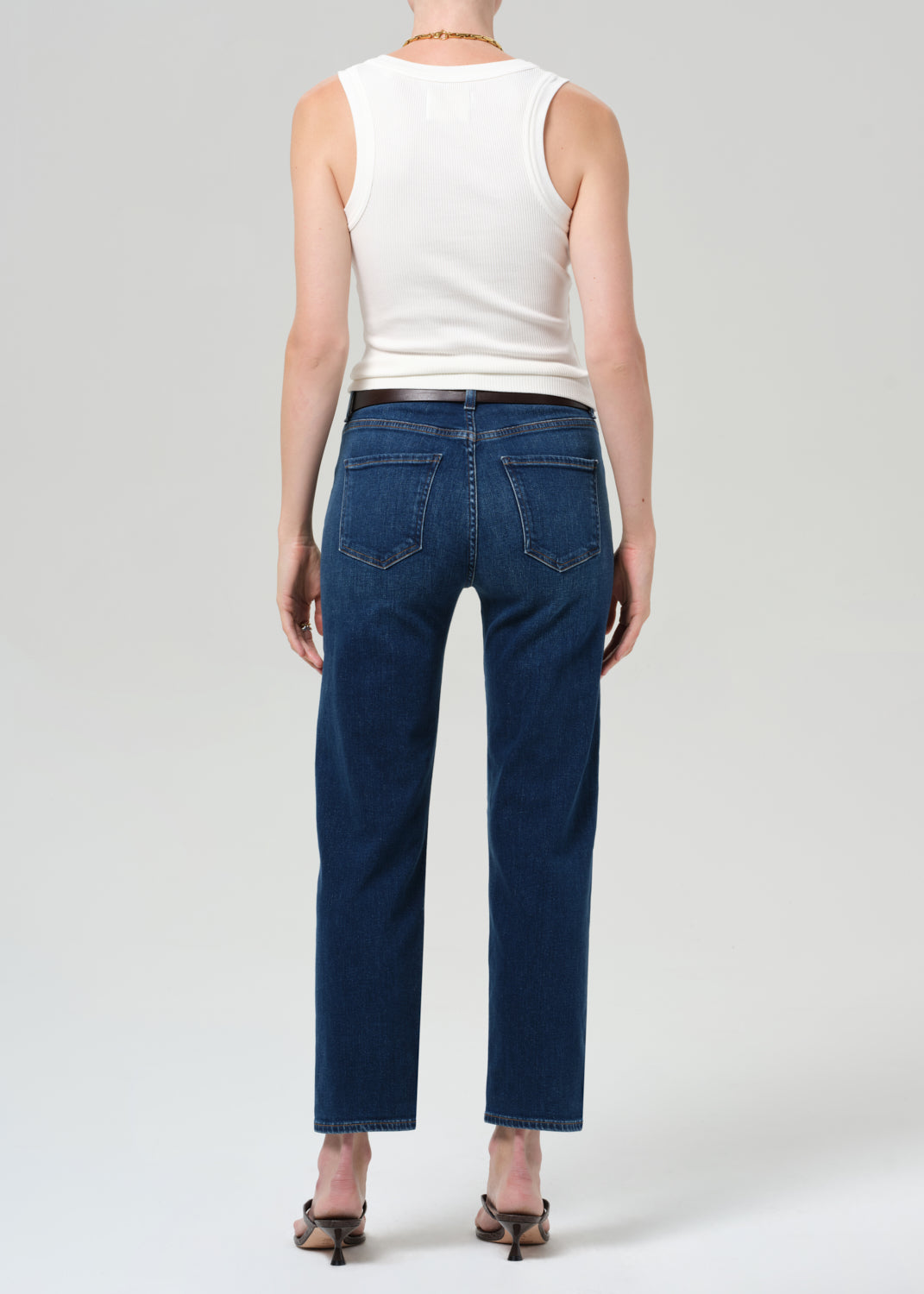 Person wearing a white sleeveless top and dark blue jeans on a light gray background