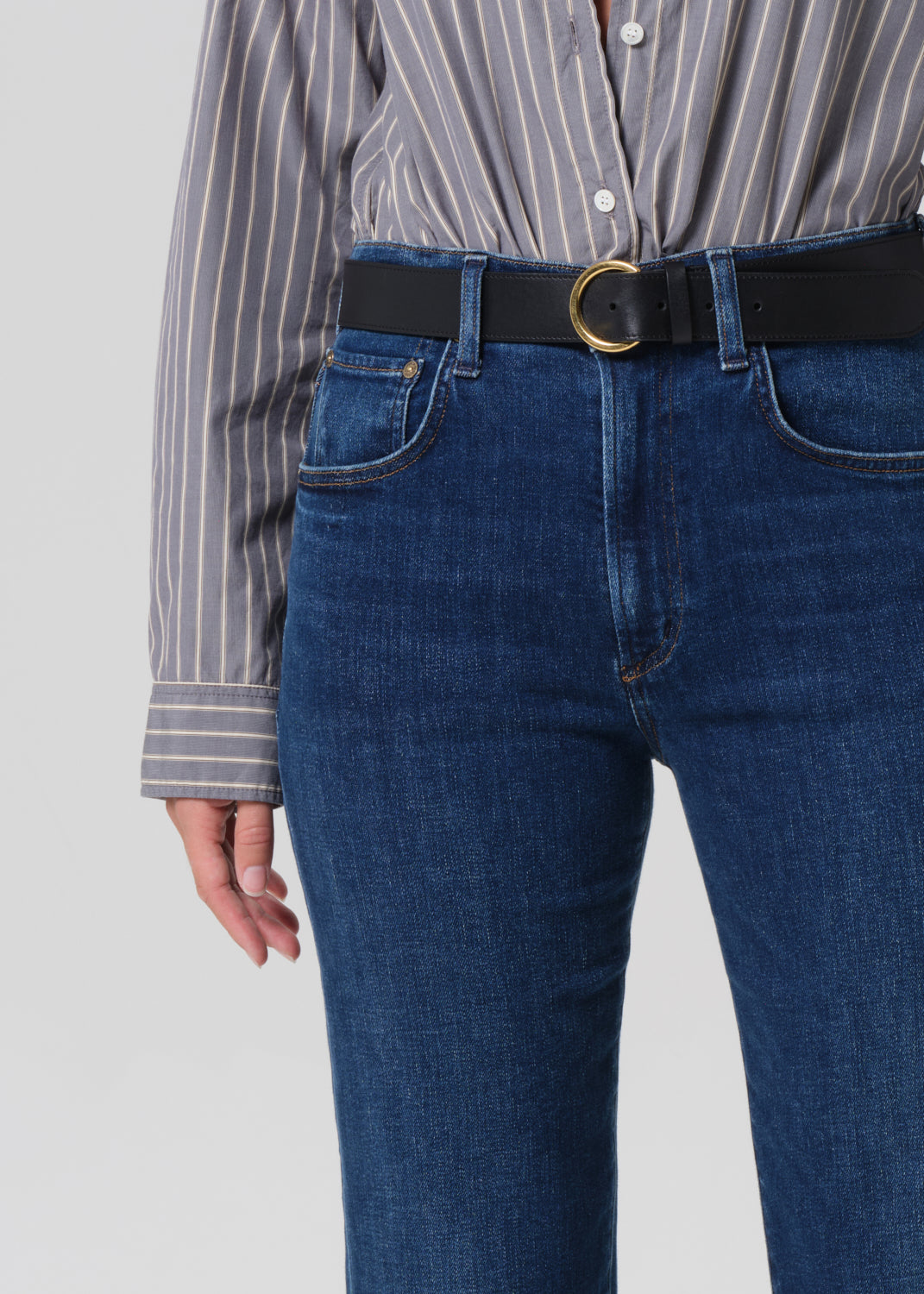 Person wearing a striped shirt and blue jeans with a black belt on a plain background