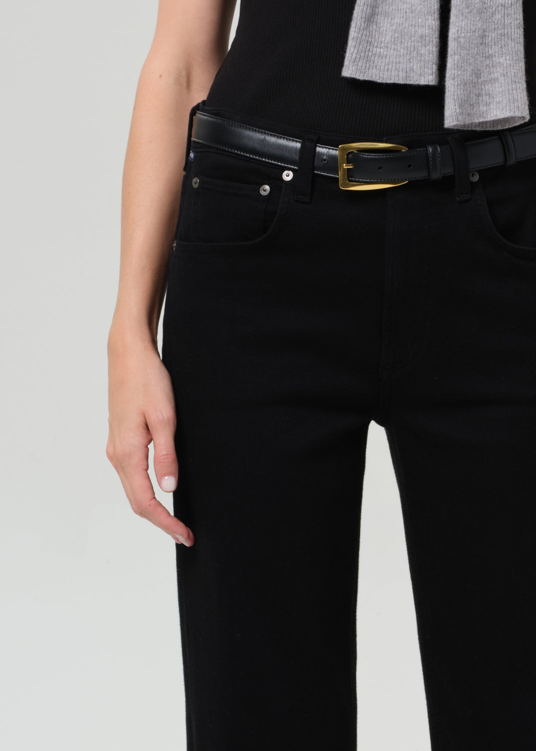 Person wearing black pants with a gold belt buckle on a light gray background