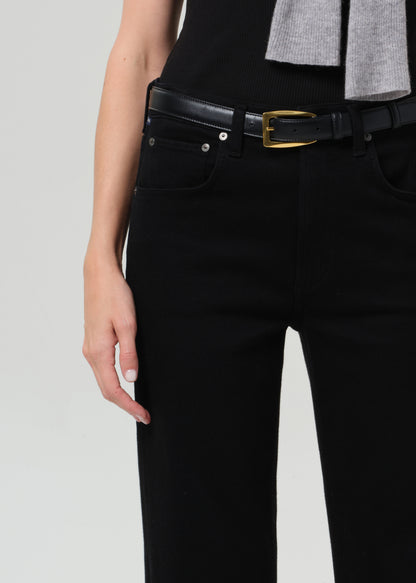 Person wearing black pants with a gold belt buckle on a light gray background