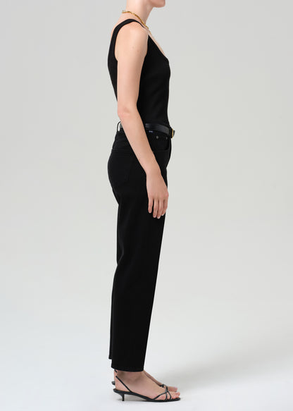 Person wearing a black sleeveless top and pants with a gray sweater, standing against a grey background