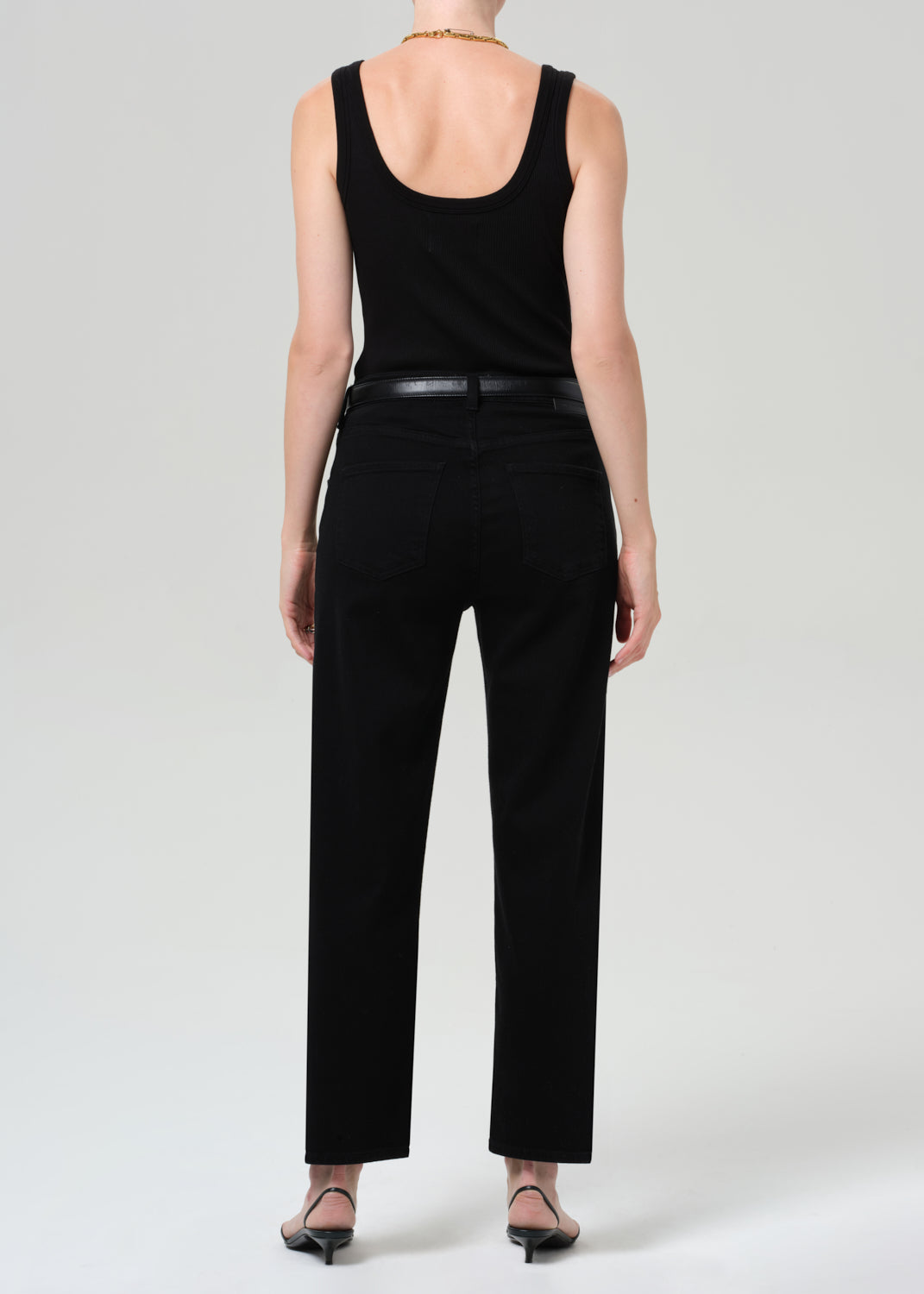 Person wearing a black sleeveless top and pants with a gray sweater, standing against a grey background