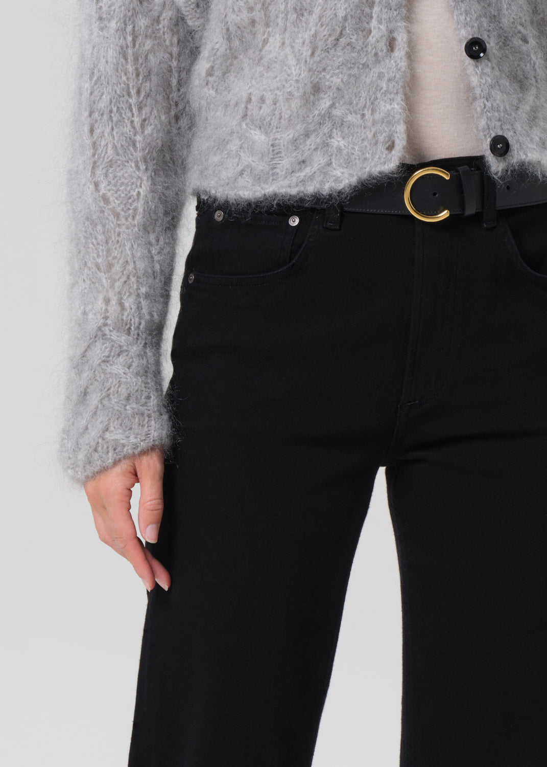 Person wearing a gray sweater and black pants on a grey background