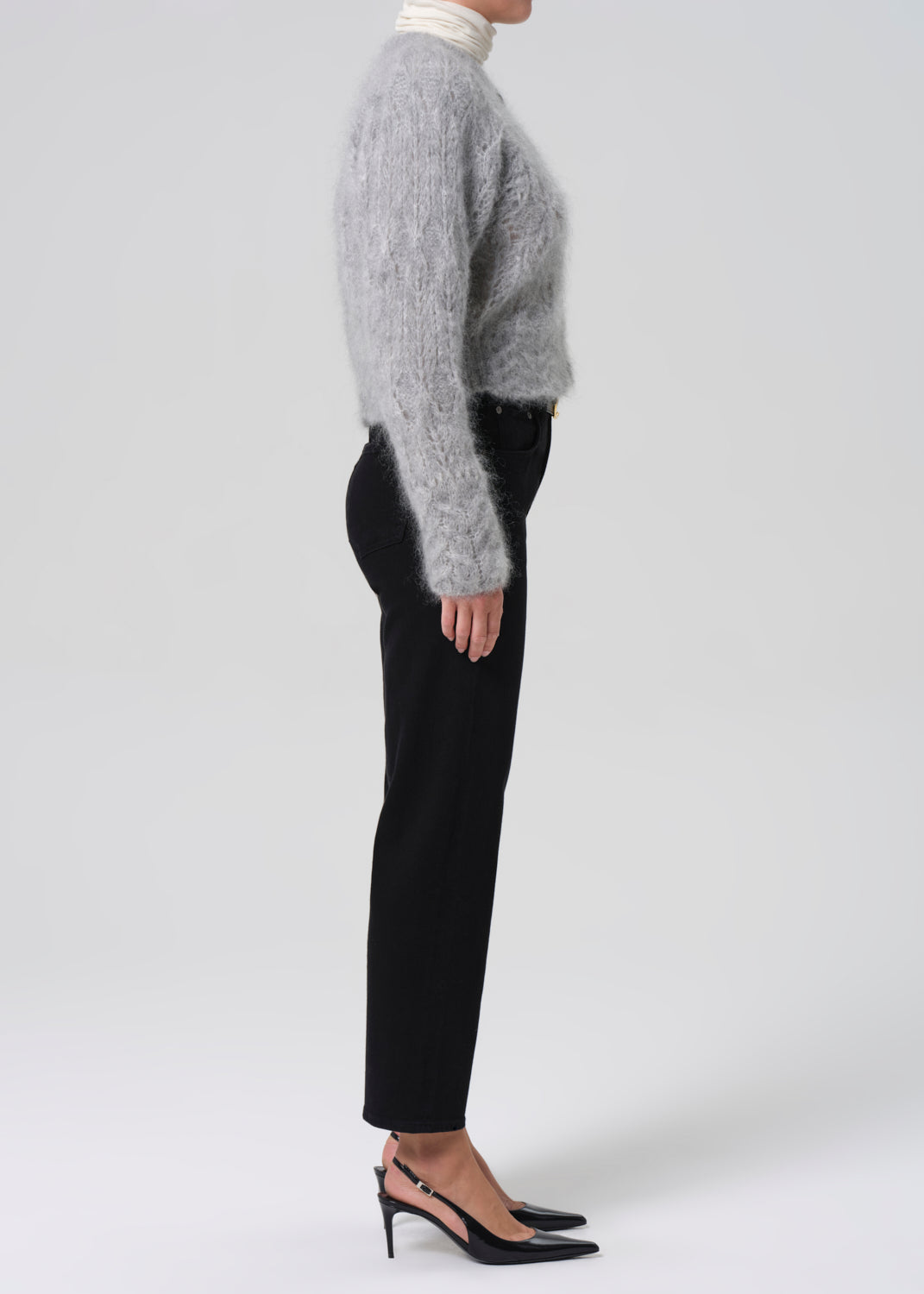 Person wearing a gray sweater and black pants on a grey background