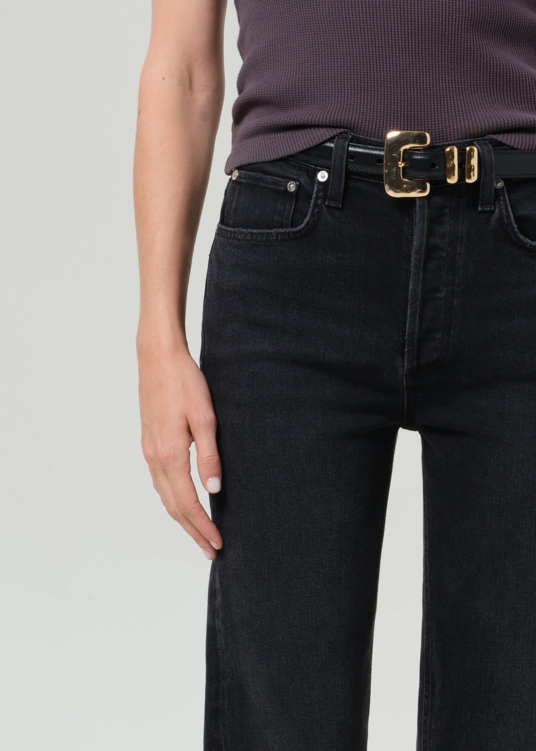 Person wearing a sleeveless top and black pants on a grey background