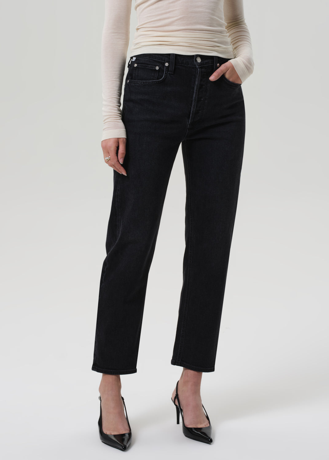 Person wearing black jeans and a beige top on a white background