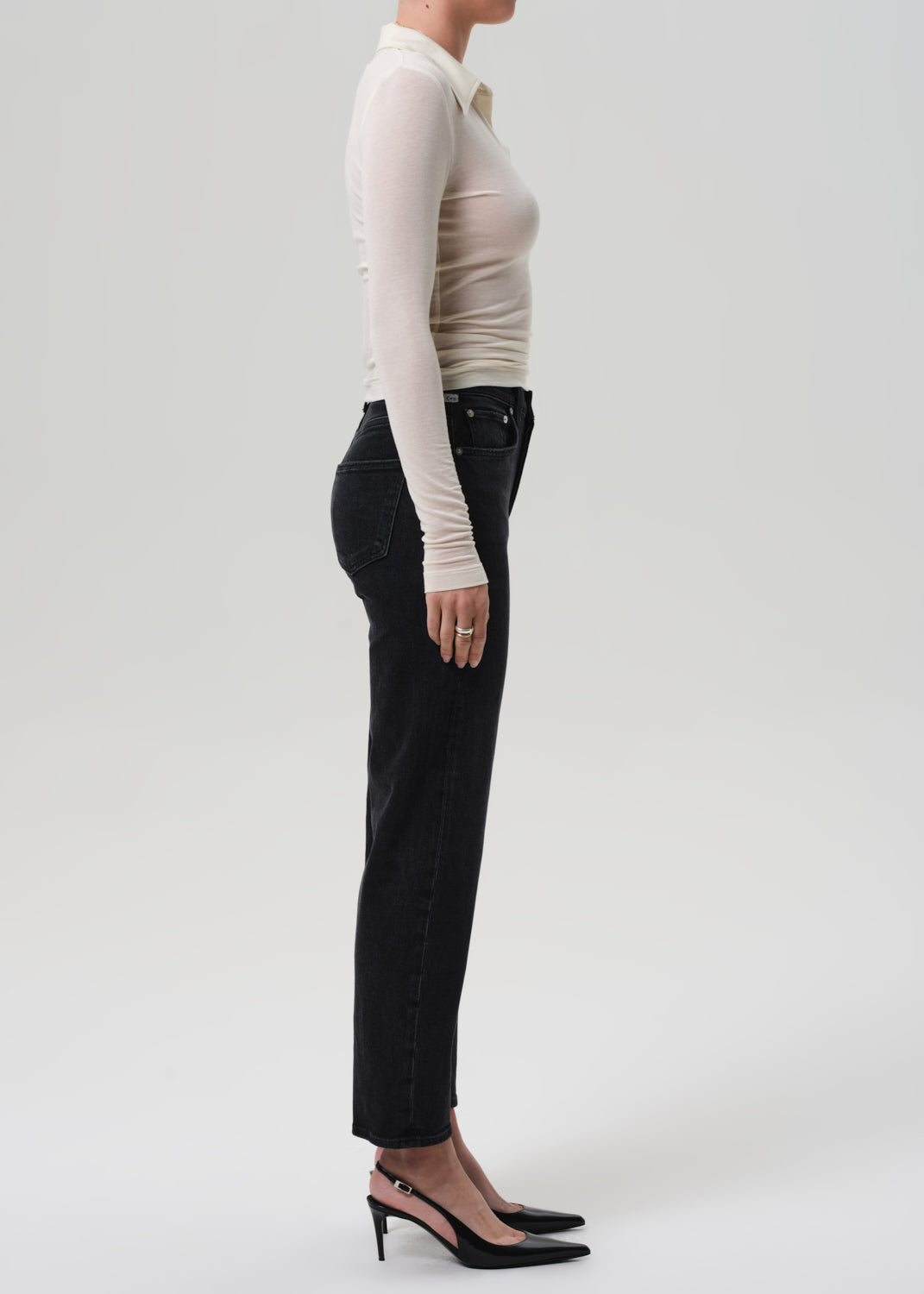 Person wearing a beige long-sleeve top and black pants on a white background