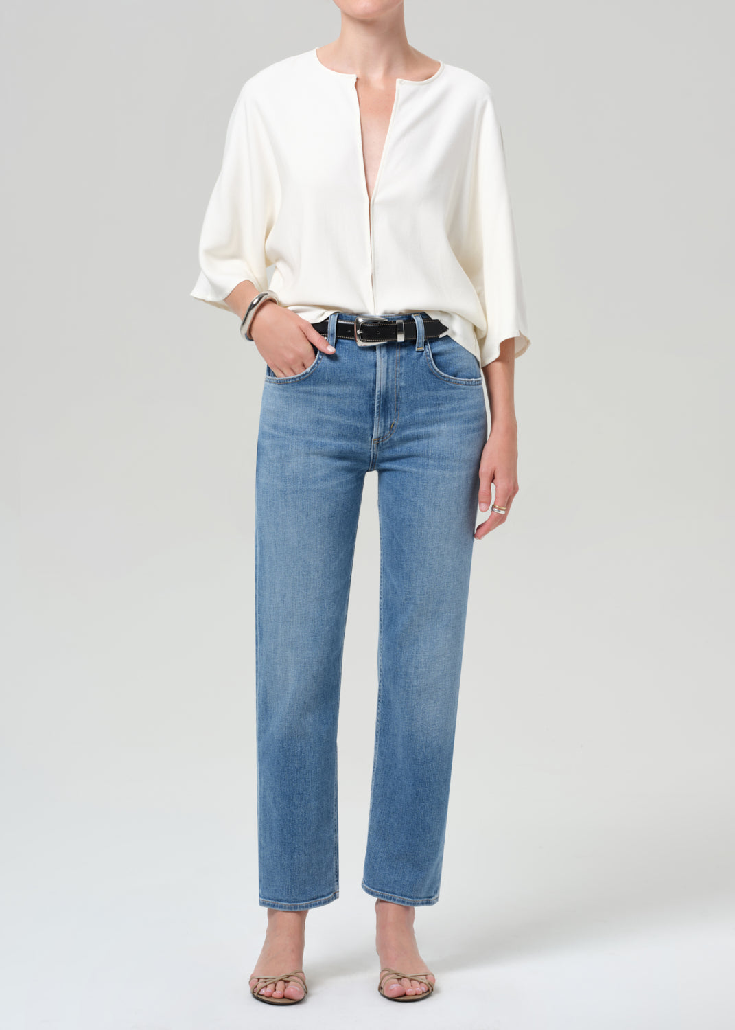 Person wearing a white blouse and blue jeans on a plain background