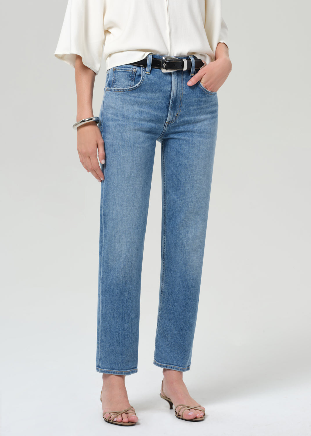 Person wearing blue jeans and a white top on a plain background