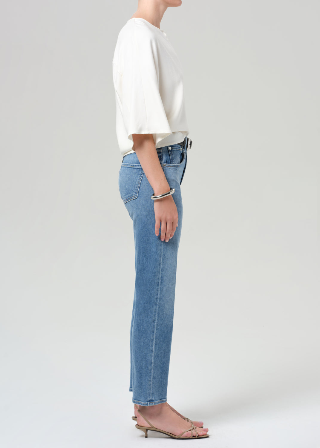 Person wearing a white top and light blue jeans on a plain background