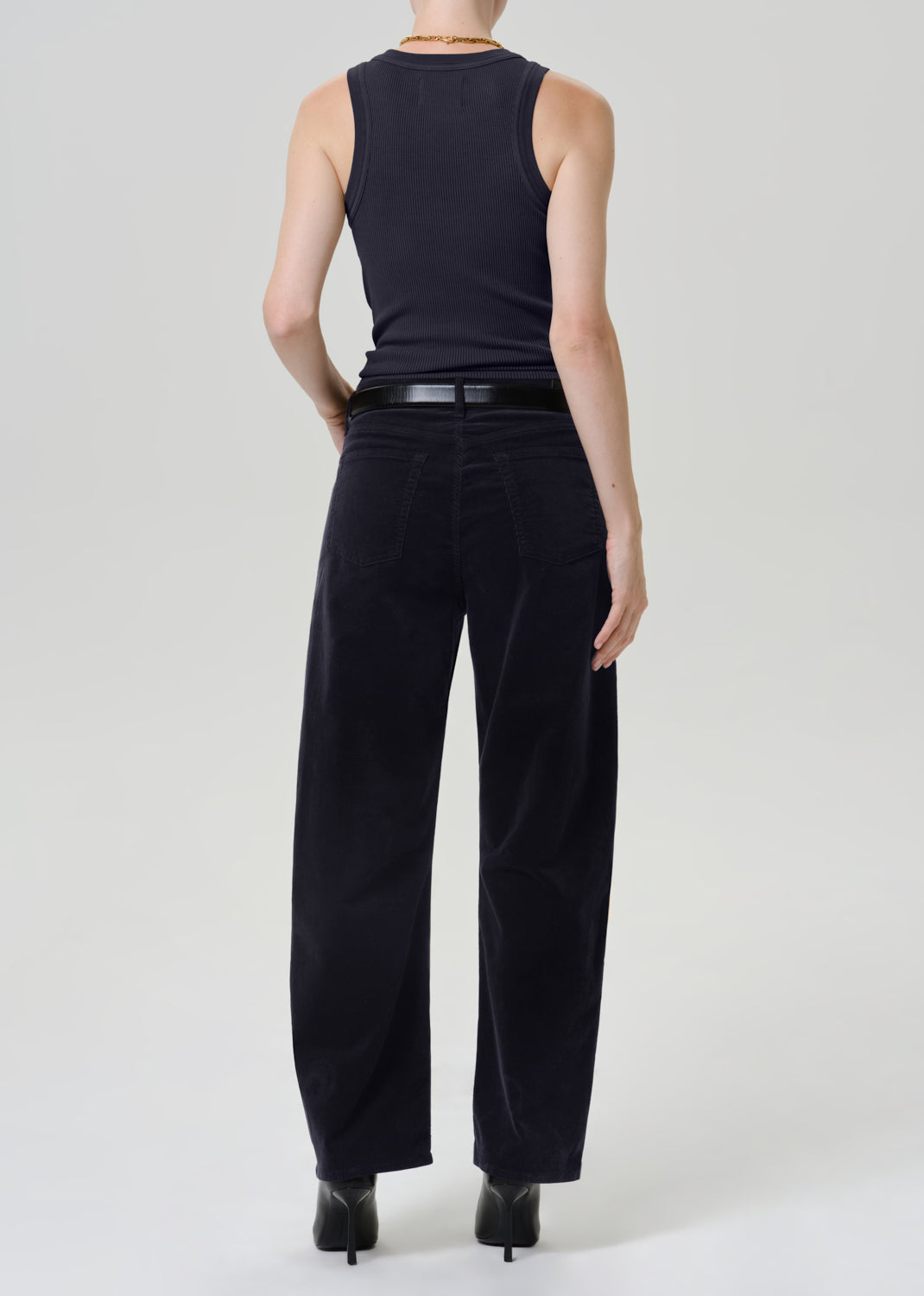 A model shown from the back wearing a dark navy sleeveless top, black wide-leg trousers, and black heels against a light gray studio background.