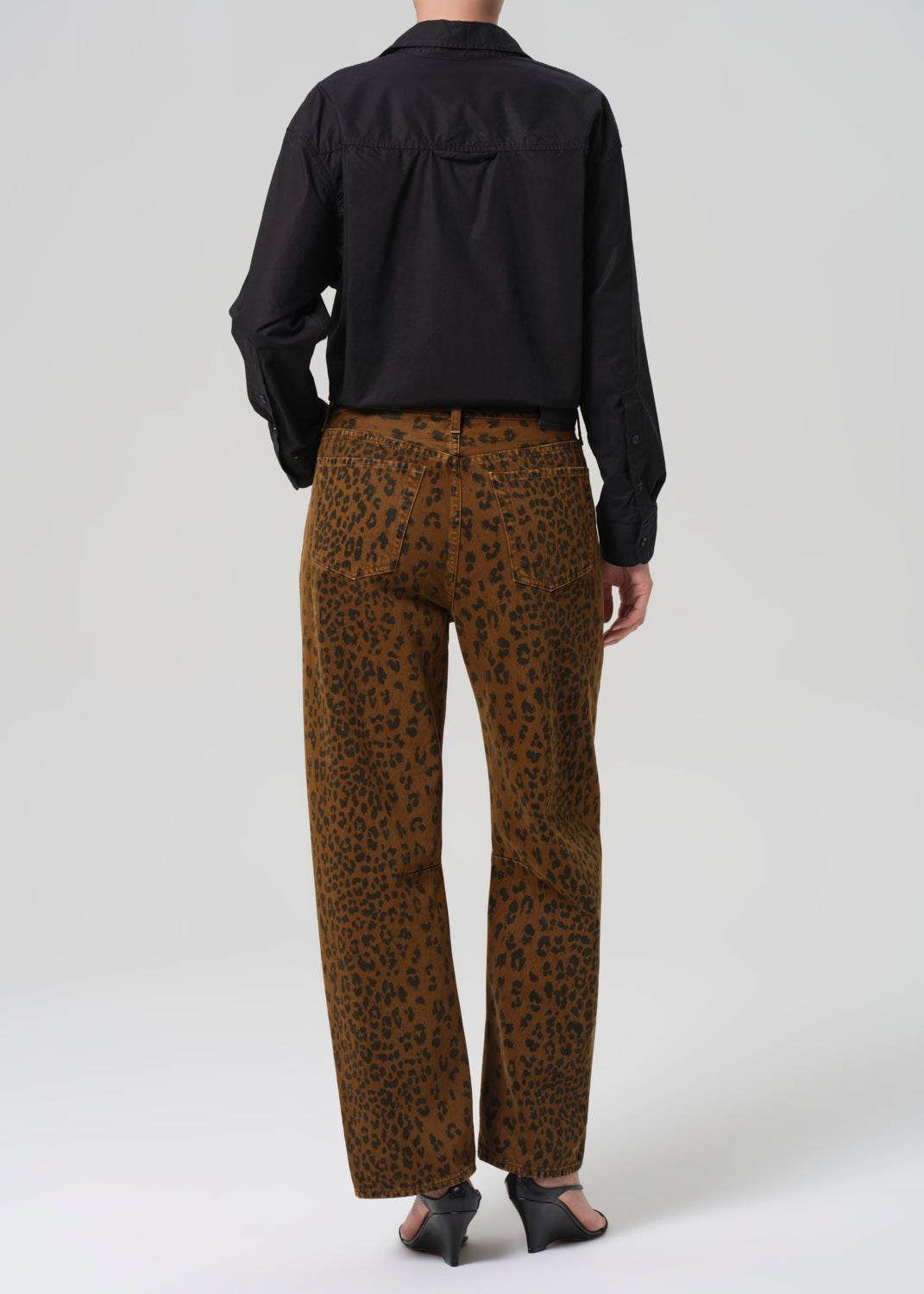 Person wearing a black shirt and brown cheetah print pants on a white background