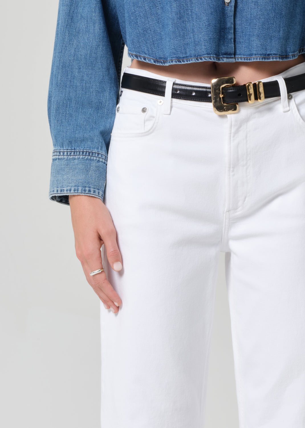 Person wearing a blue denim shirt and white pants with a black belt.