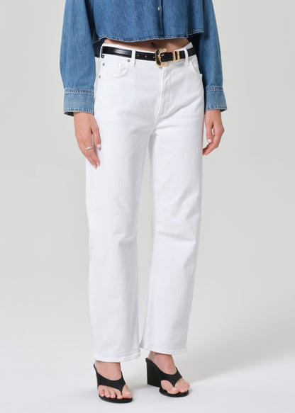 Person wearing white jeans with a denim shirt and black sandals on a plain background