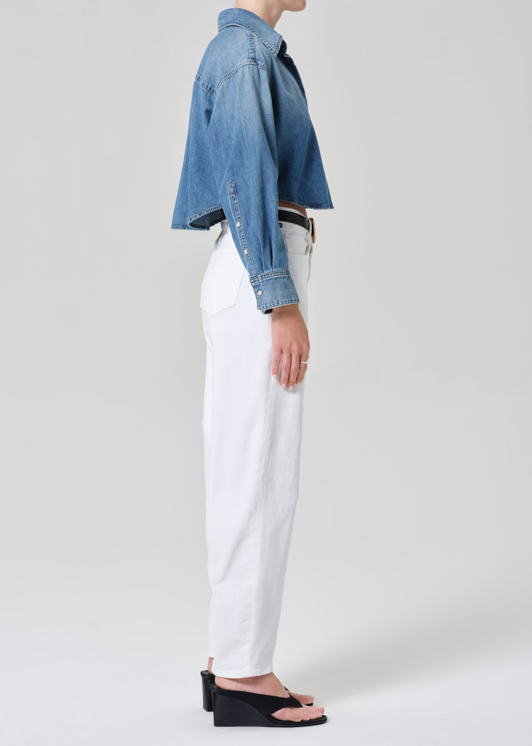 Person wearing a denim jacket and white pants on a plain background
