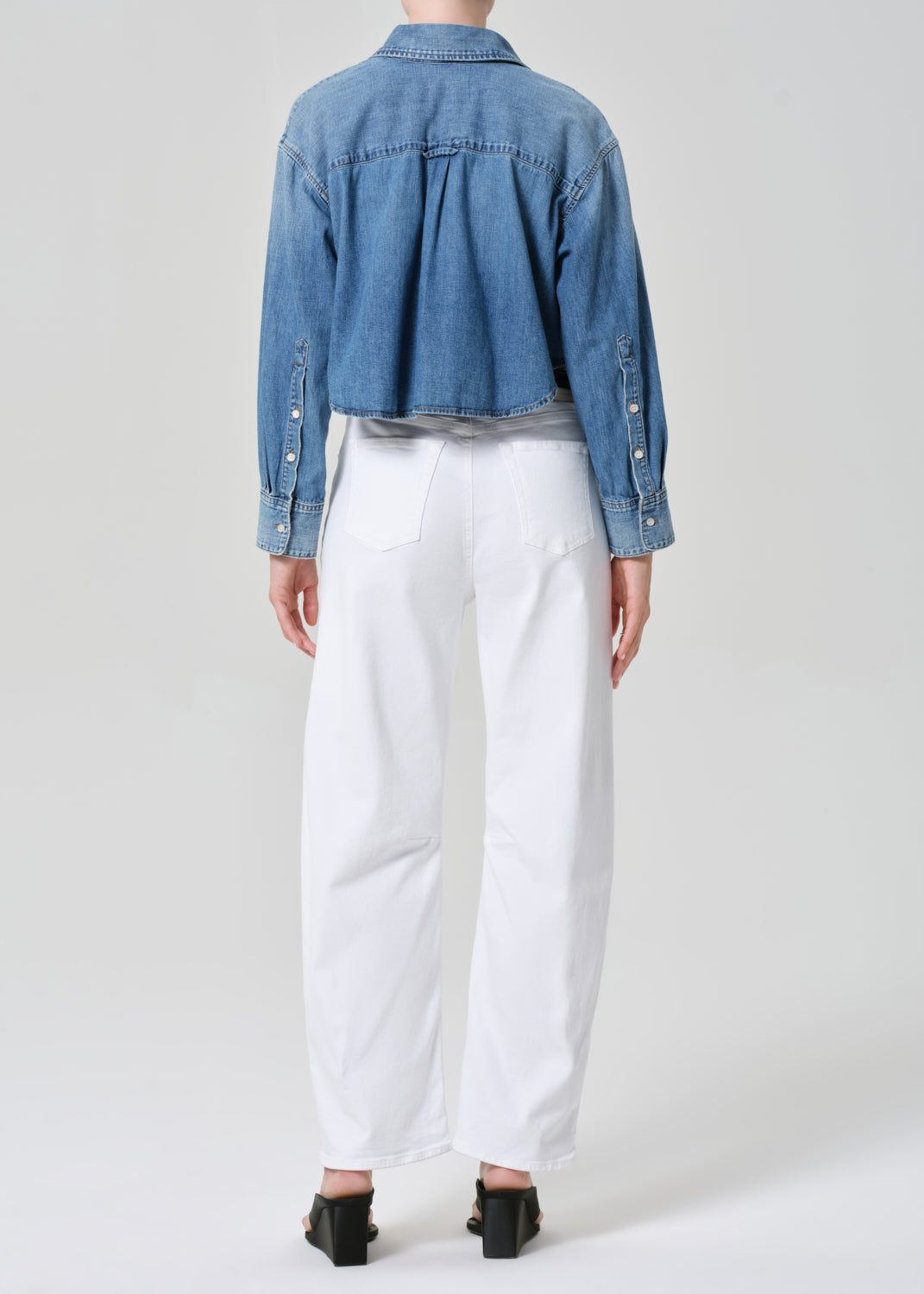 Person wearing a blue denim jacket and white pants on a plain background