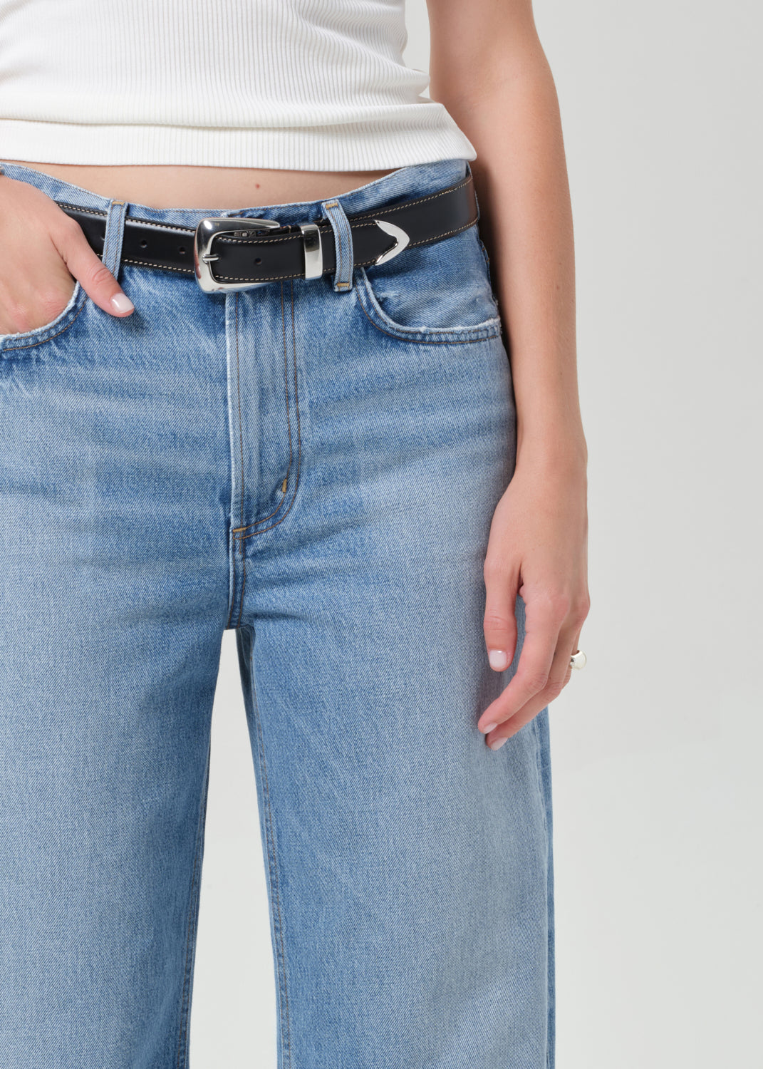 Person wearing blue jeans with a black belt on a plain background