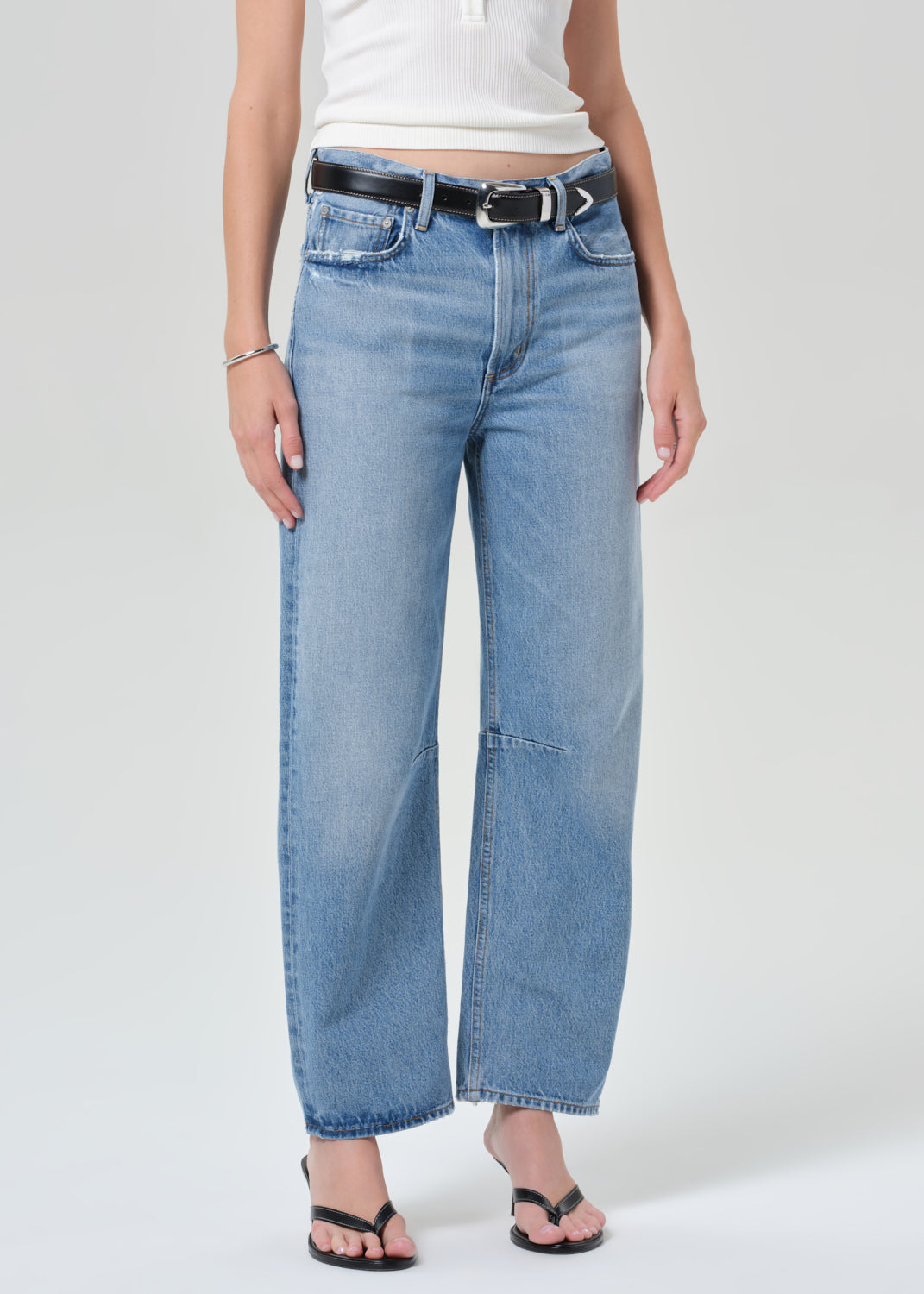 Person wearing light blue jeans and a white top on a plain background