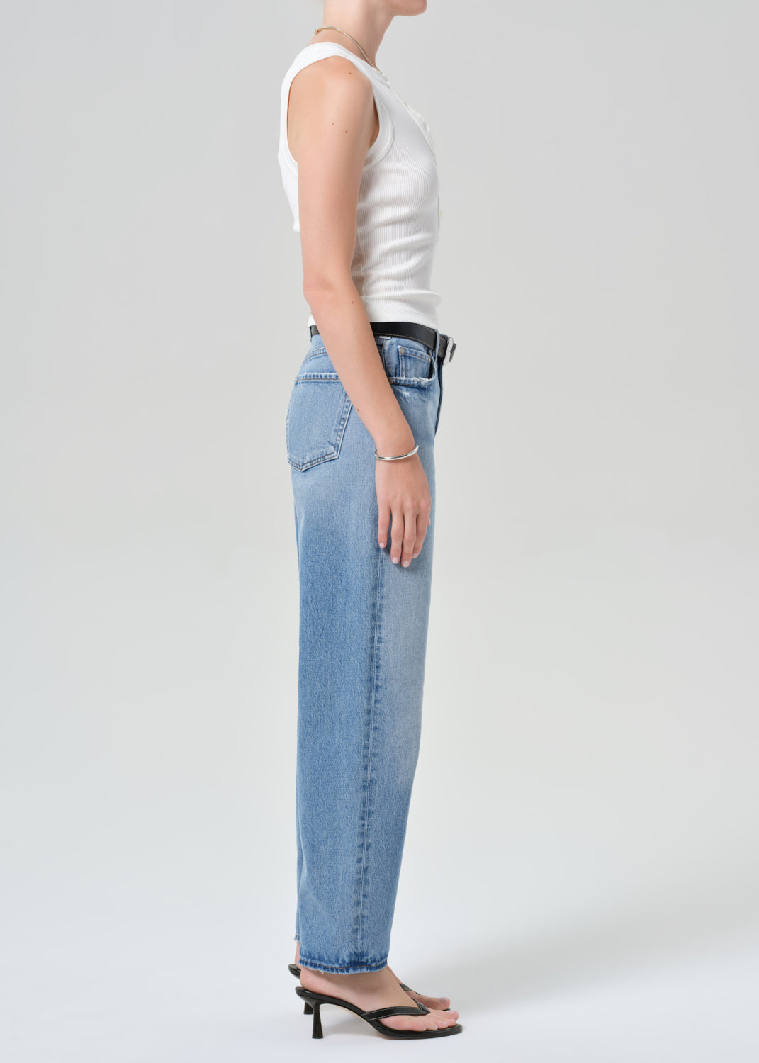 Person wearing light blue jeans and a white top on a plain background
