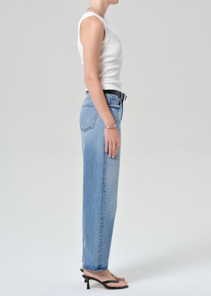 Person wearing light blue jeans and a white top on a plain background
