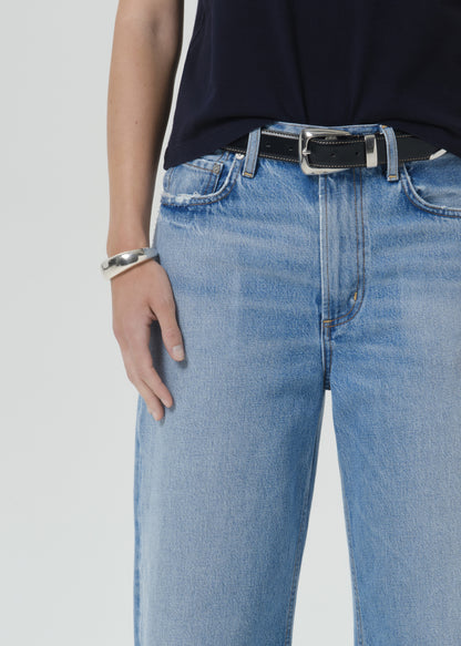 Close-up of a person wearing light blue denim jeans with a black leather belt featuring a silver buckle, paired with a dark top and a silver bracelet.