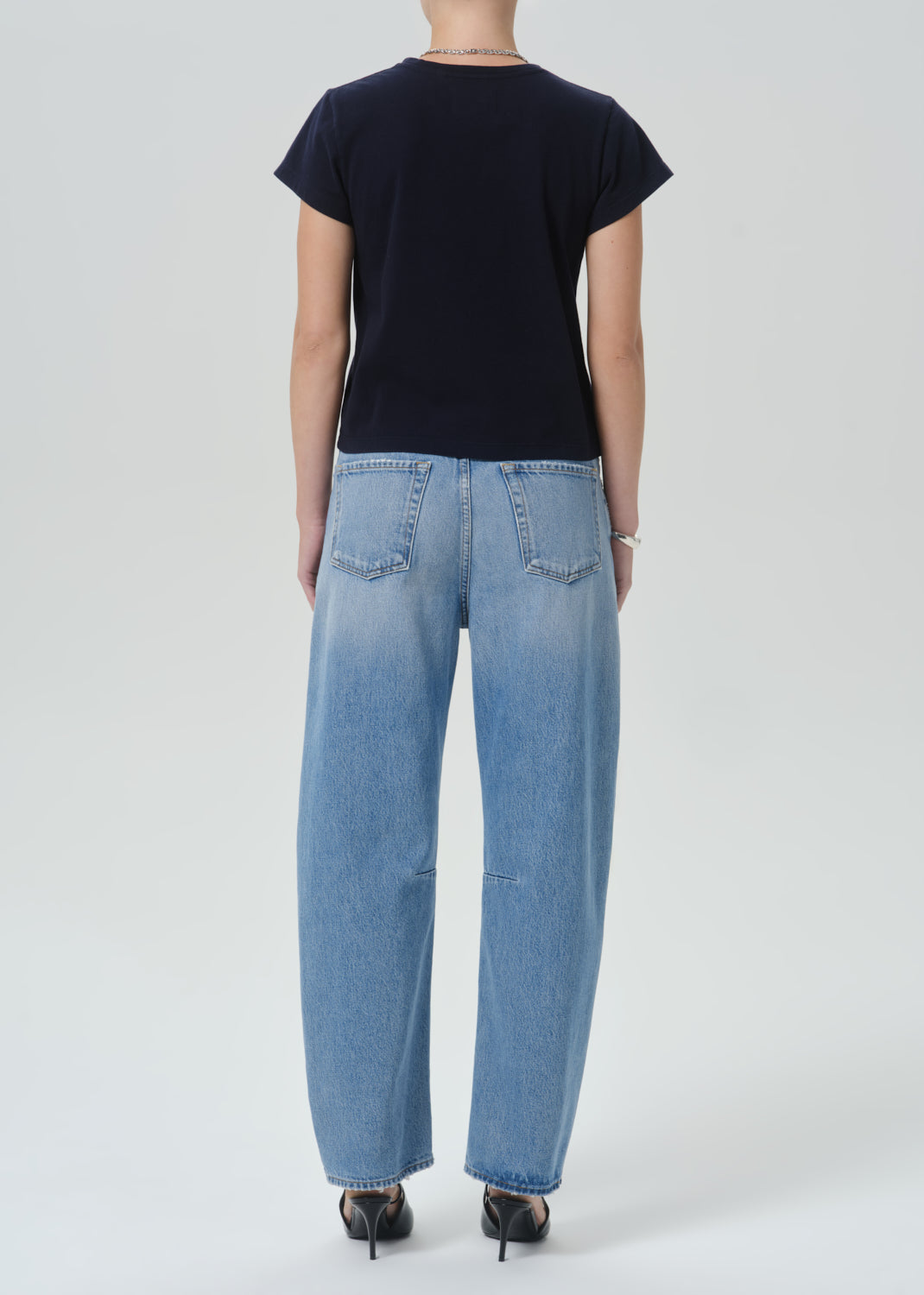 A model shown from the back wearing a dark navy t-shirt and light blue wide-leg denim jeans, paired with black heels, against a grey background.