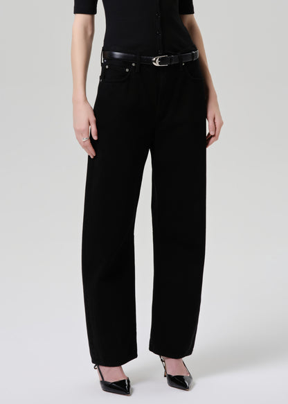 A model wearing black wide-leg cropped jeans with a black belt, paired with a black short-sleeve top and black pointed-toe heels, photographed against a grey background.