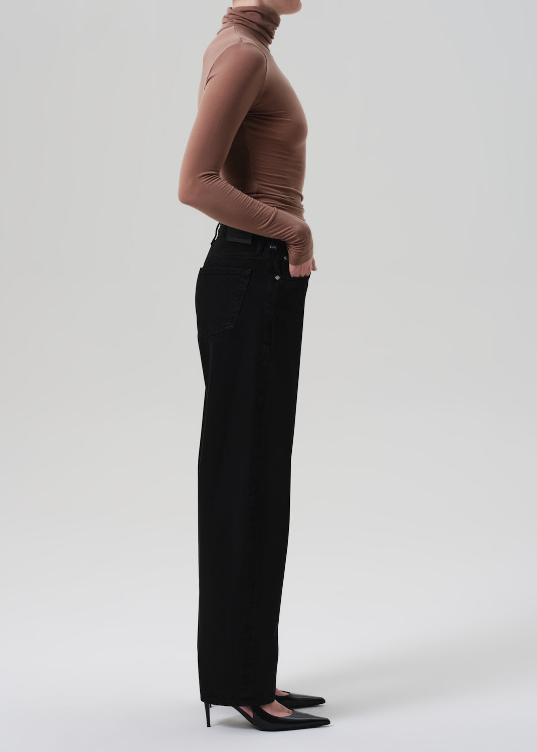 Person wearing a brown turtleneck and black pants on a white background