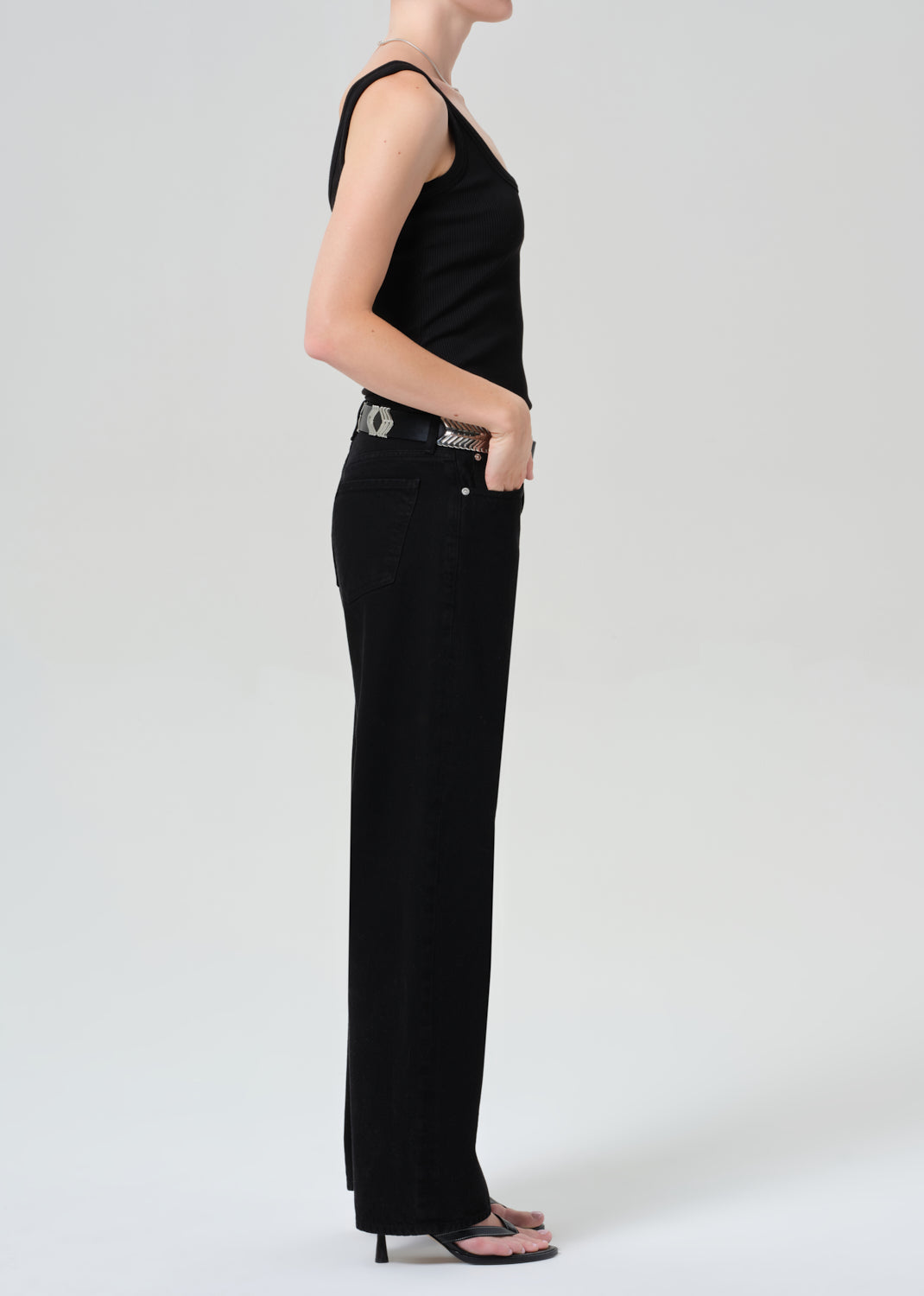 Person wearing a black sleeveless top and black jeans on a plain background