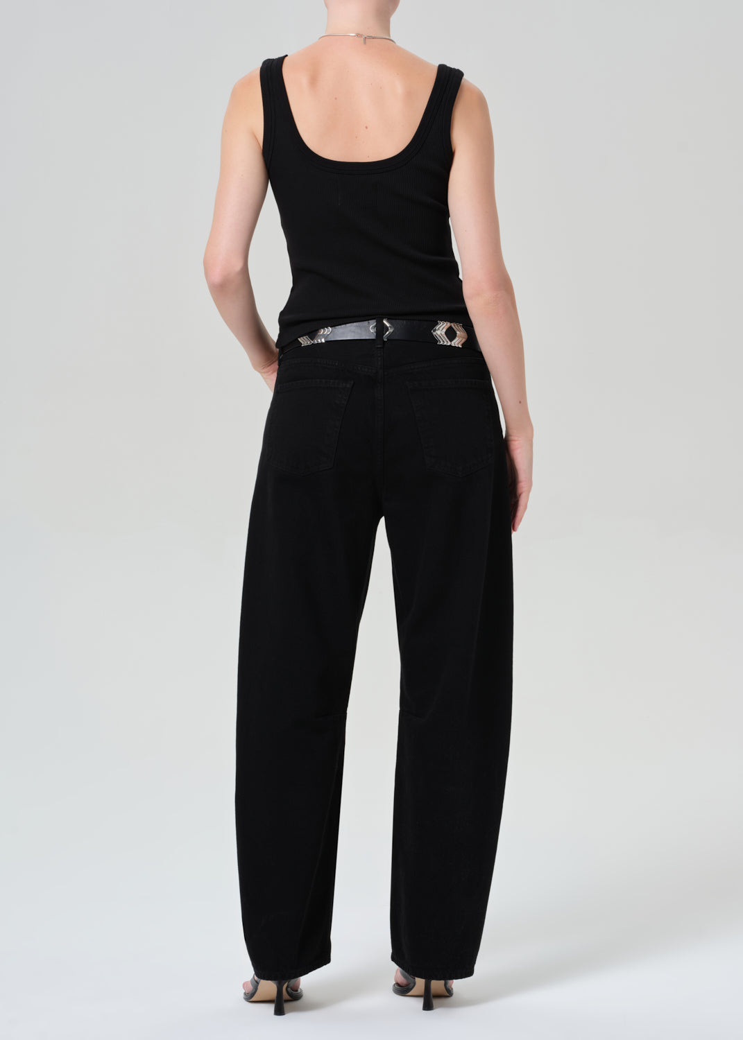 Person wearing a black sleeveless top and black jeans on a plain background