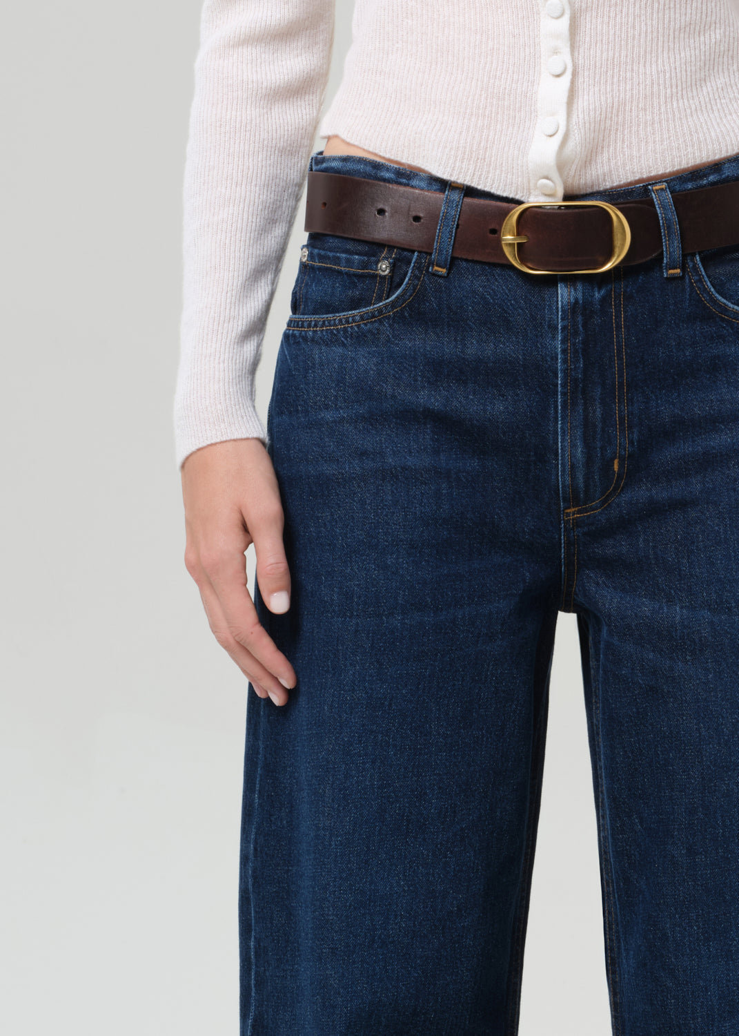 Person wearing blue jeans with a brown belt on a plain background