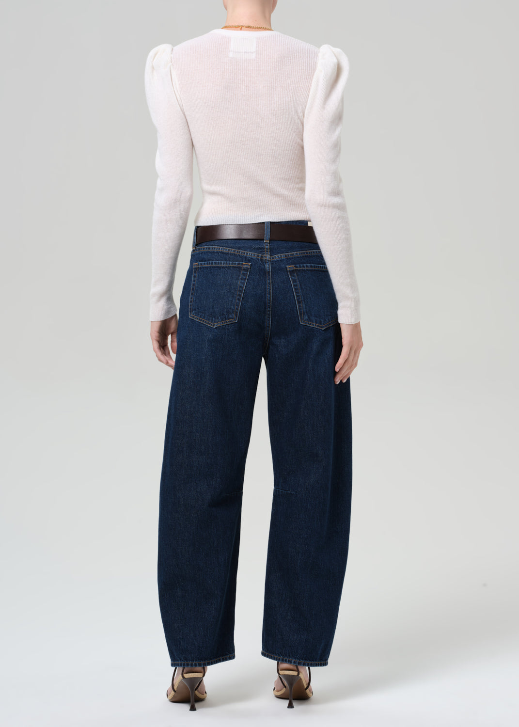 Person wearing a white long-sleeve top and dark blue jeans on a plain background