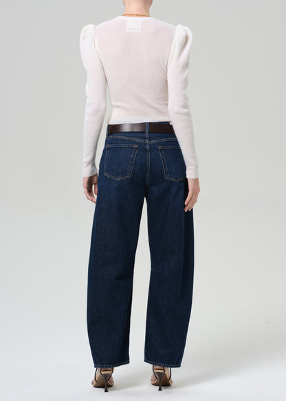 Person wearing a white long-sleeve top and dark blue jeans on a plain background