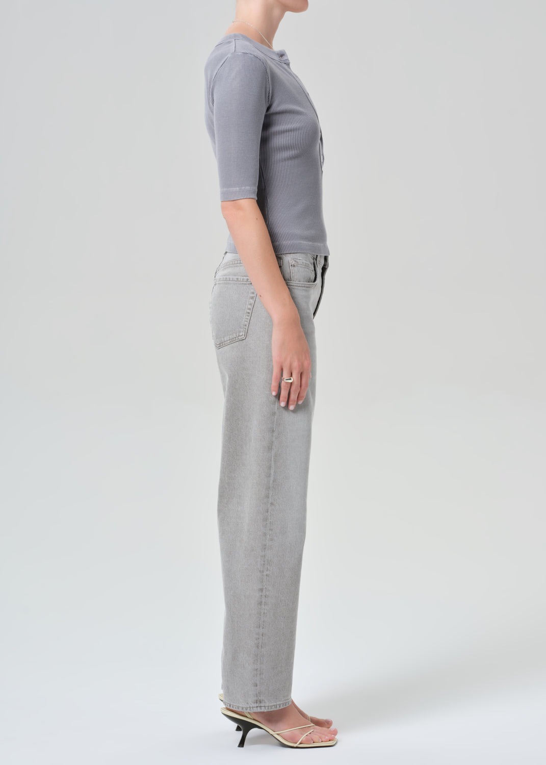 Person wearing a gray top and light gray jeans on a plain background
